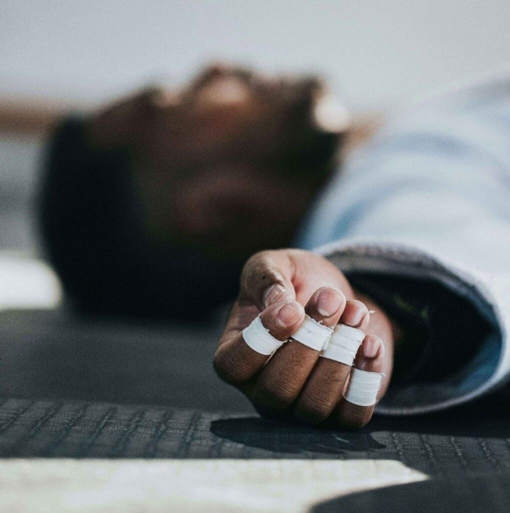 Close-up of an exhausted athlete's taped fingers lying on a gym floor after intense training.
